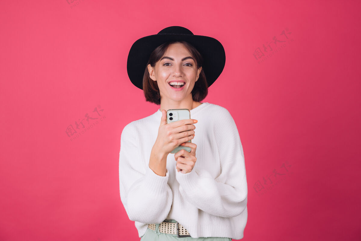 美丽穿着白色休闲毛衣 戴着红粉色帽子的时髦女人互联网姿势快乐
