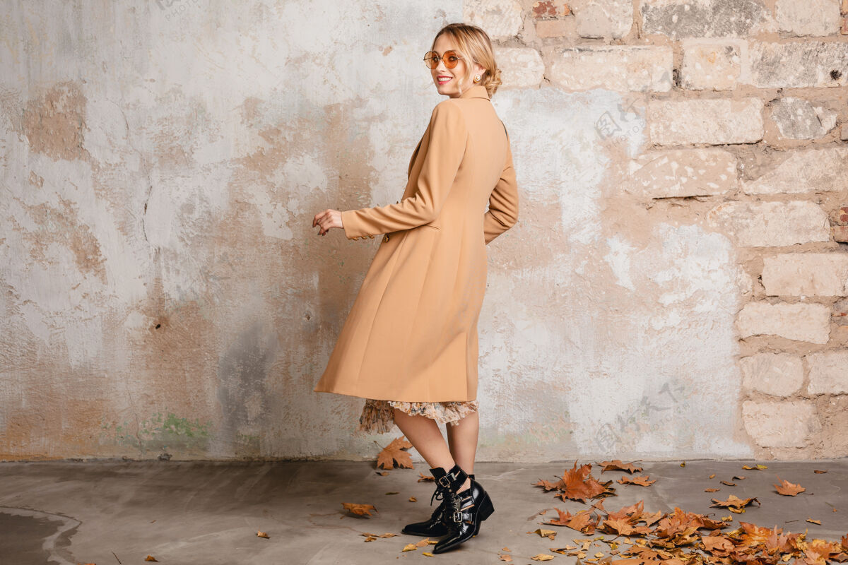 衣服穿着米色外套的迷人时尚金发女人在街上靠着老式的墙走着城市靴子秋天