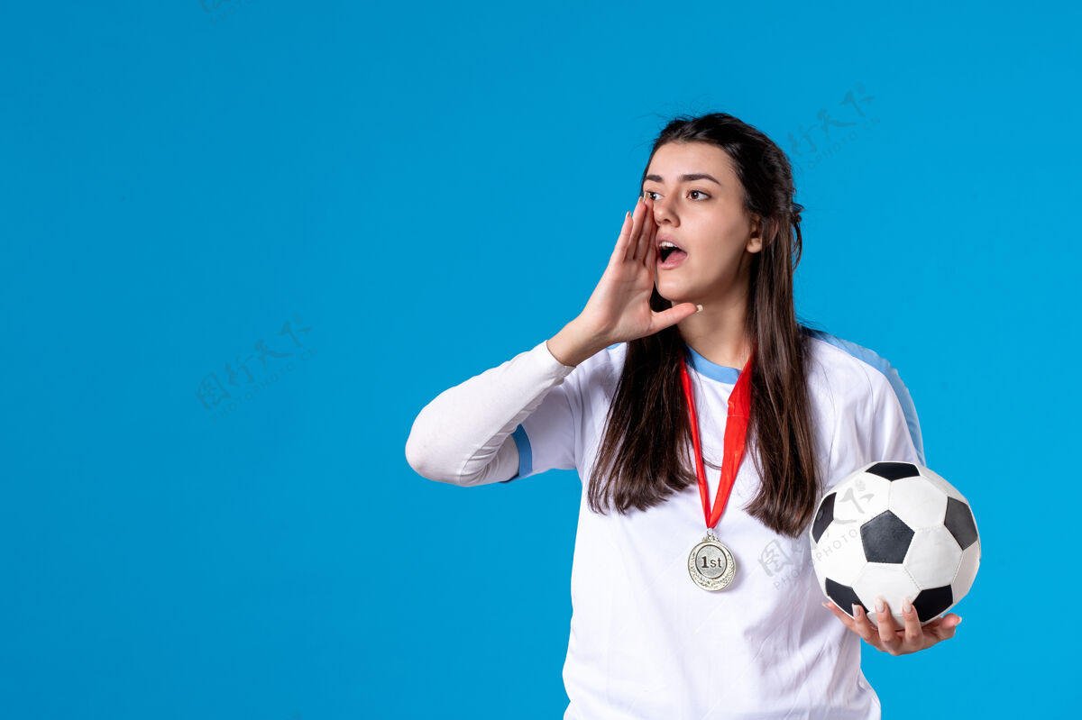 手持前视图：年轻女子在蓝色墙上拿着足球足球体育年轻人