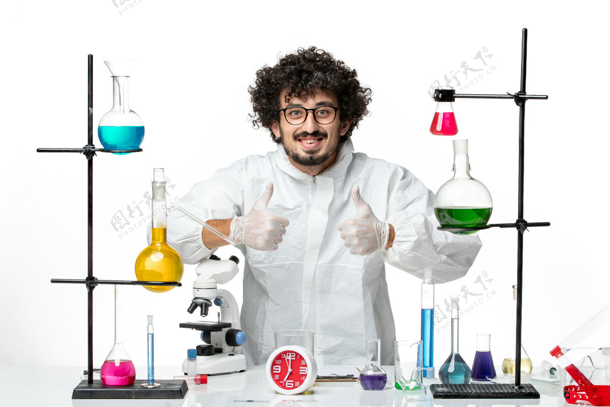 立场正面图身穿特殊套装的年轻男性科学家站在桌子周围 白色的墙上有解决方案烧杯外套特殊