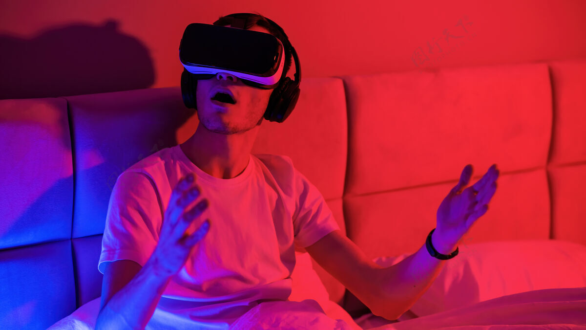 眼镜这个年轻人戴着一副蓝色和红色的虚拟现实眼镜 躺在床上的房间里 给人留下了深刻的印象游戏运动未来派