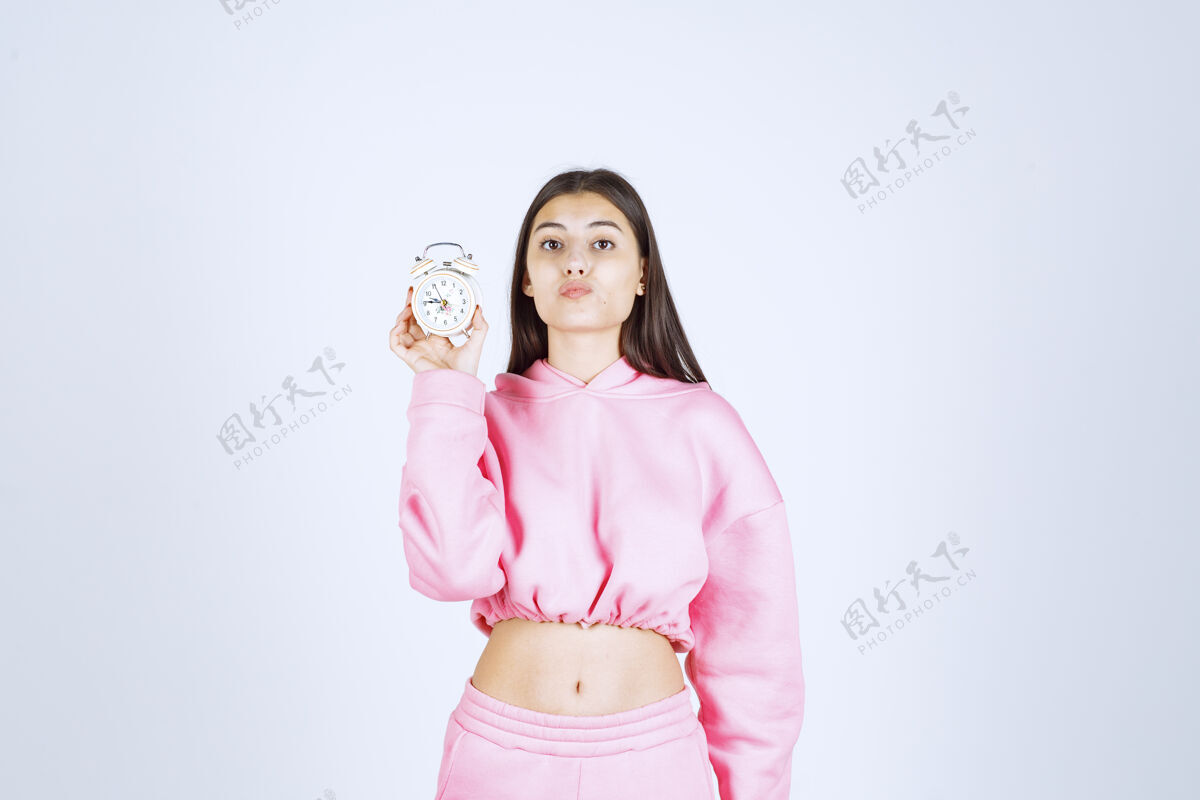 方便一个穿着粉色睡衣的女孩拿着一个闹钟 把它当作一个产品来推销员工人服装