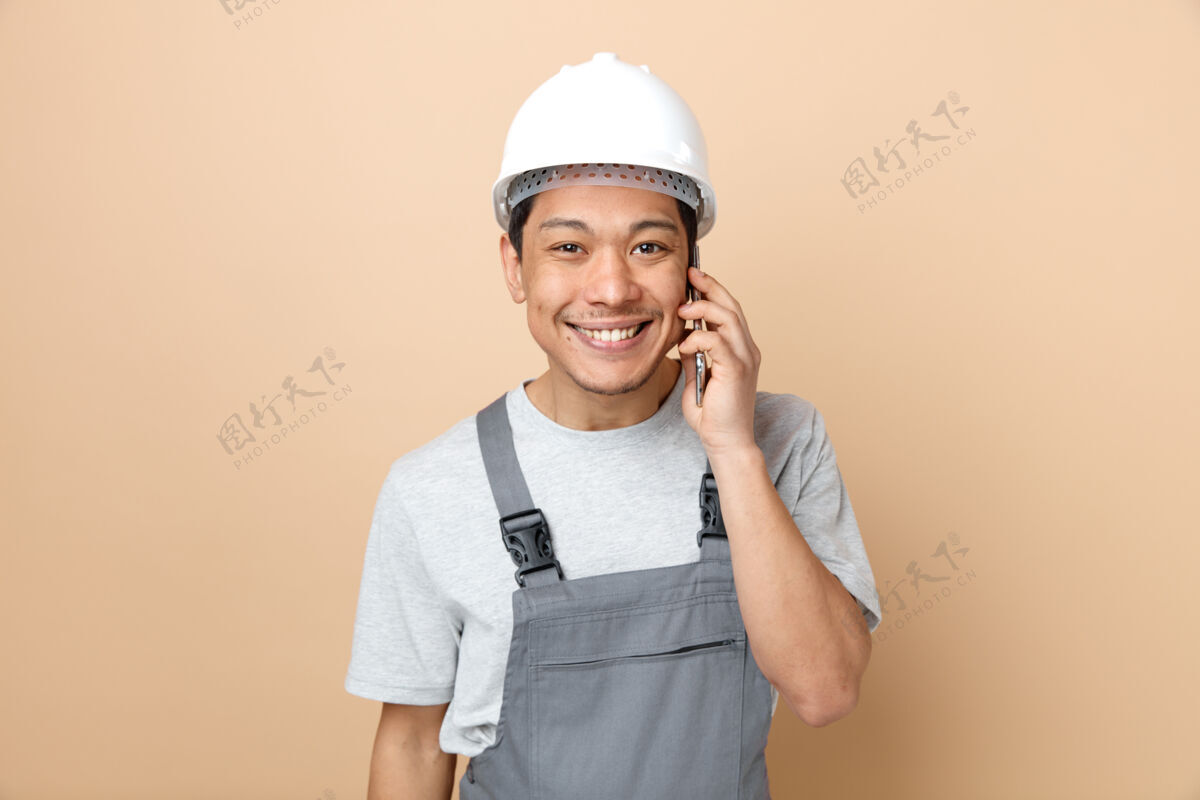 工人微笑着戴着安全帽和制服的年轻建筑工人在打电话年轻头盔奶油