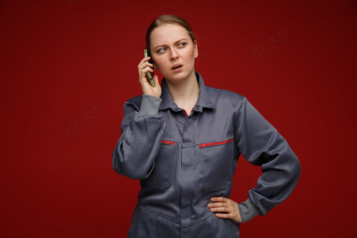 混乱困惑的年轻金发女工程师穿着制服讲电话 手放在腰上看着身边金发工程师壁板