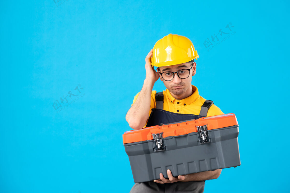 盒子悲伤的男建筑工人的正面图 他手上拿着蓝色的工具箱手建筑建筑工人