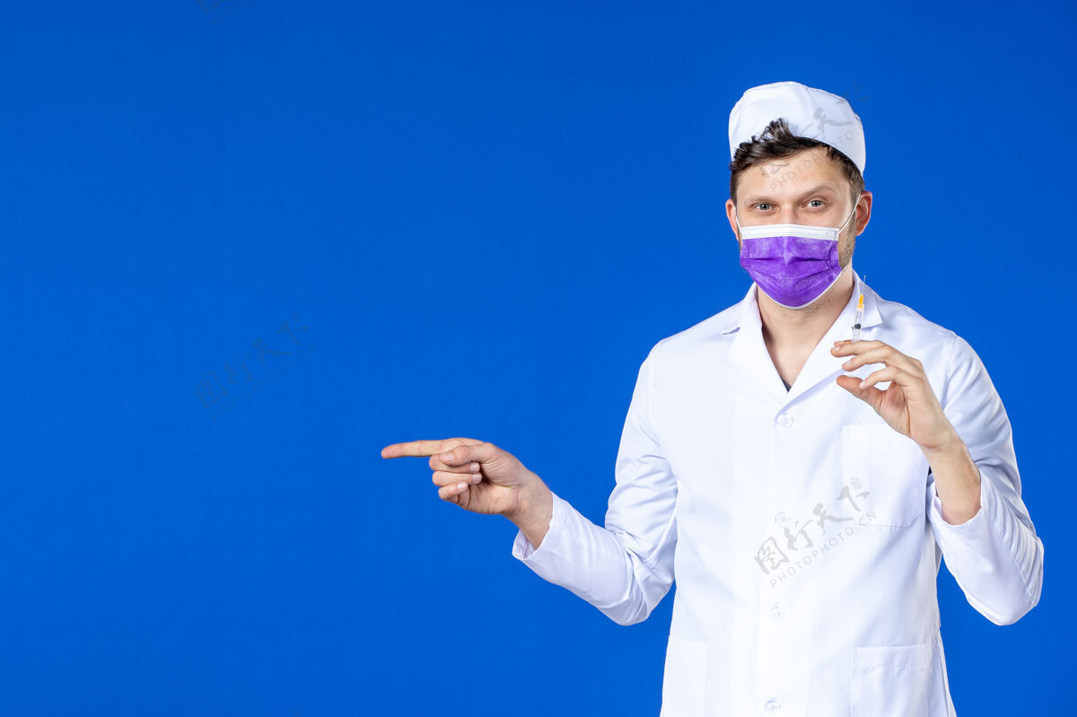 男医生前视图中的男医生穿着医疗服和口罩持有疫苗和注射在蓝色药品疫苗注射剂