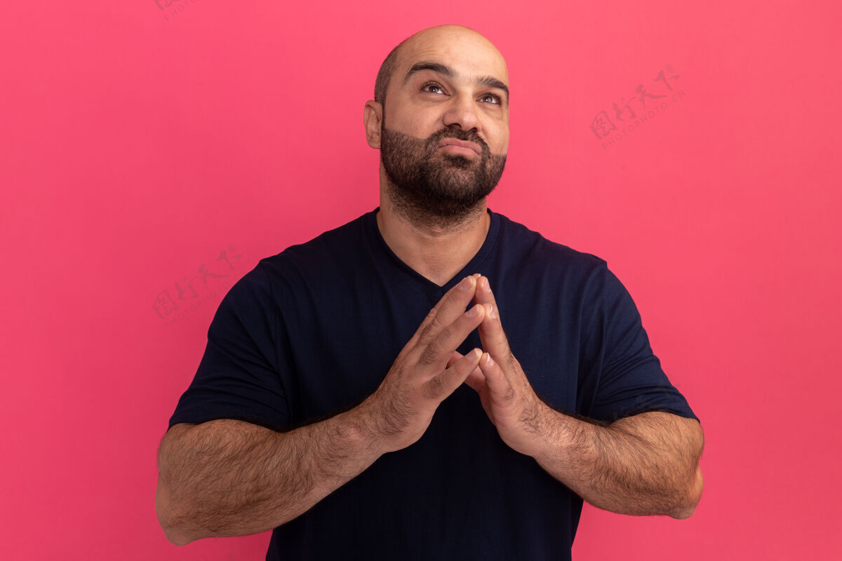 喜欢一个留着胡子的男人穿着海军蓝t恤 手拉着手 像是在祈祷 带着希望的表情站在粉色的墙上男人胡子表情
