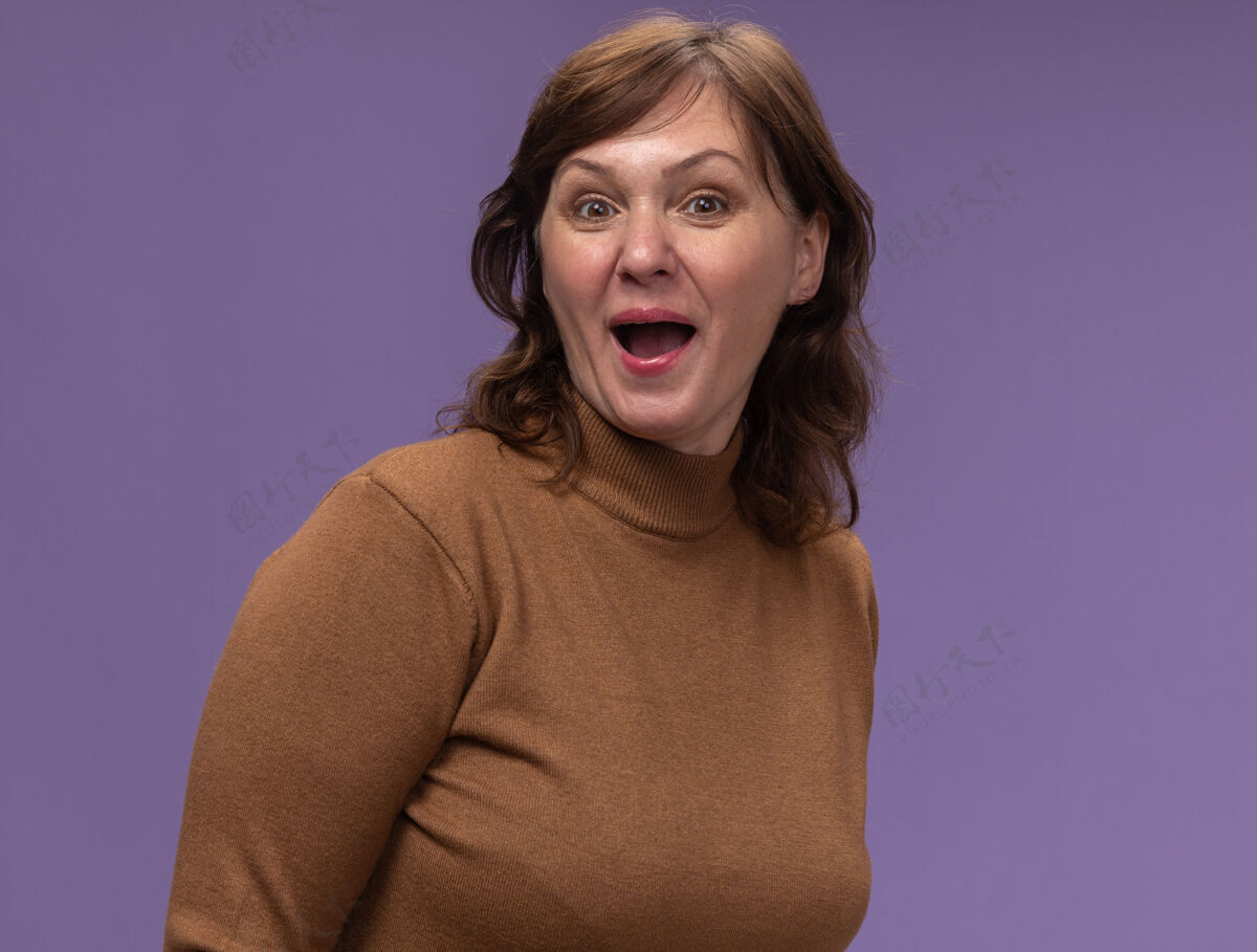 女人一位穿着棕色高领毛衣的中年妇女站在紫色的墙上 脸上洋溢着幸福和惊喜年龄中等惊喜