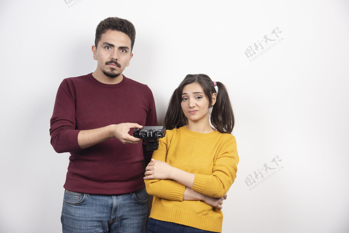 休闲一个男人在白墙上给一个年轻的女人一个相机年轻人男人女人