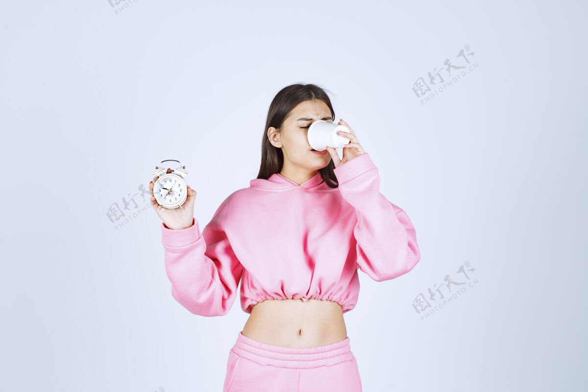 茶穿着粉色睡衣的女孩拿着闹钟 喝着一杯咖啡雇员工作人员人类