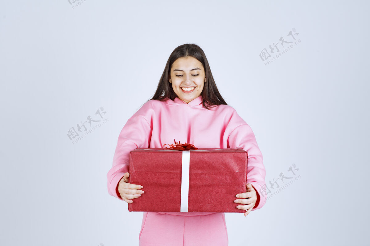 员工穿着粉色睡衣的女孩抱着一个大大的红色礼盒 微笑着服装晋升聪明