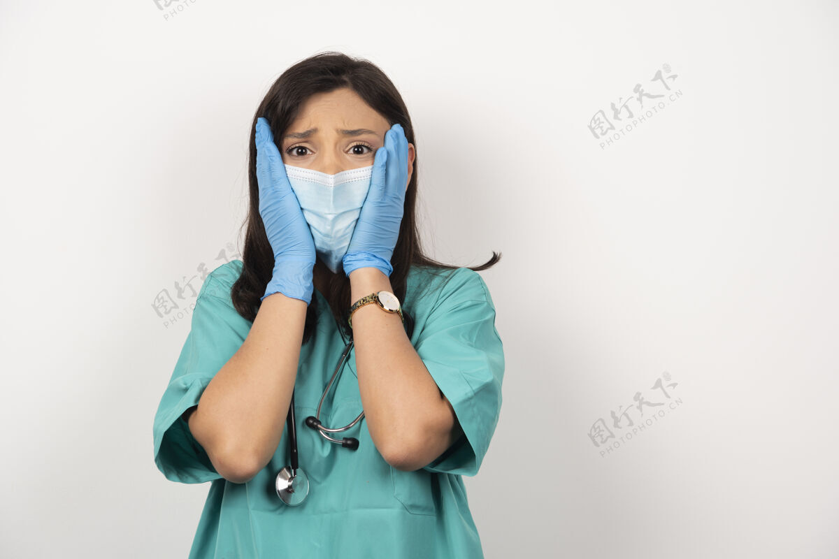 职业医生戴着医用面罩和手套 脸上挂着白色的背景 吓坏了她医疗女性医生