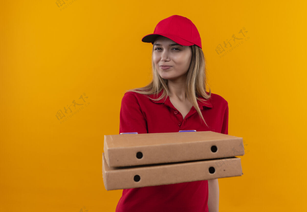 请穿高兴的年轻女送货员穿着红色制服 戴着帽子 手里拿着比萨饼盒制服披萨年轻人