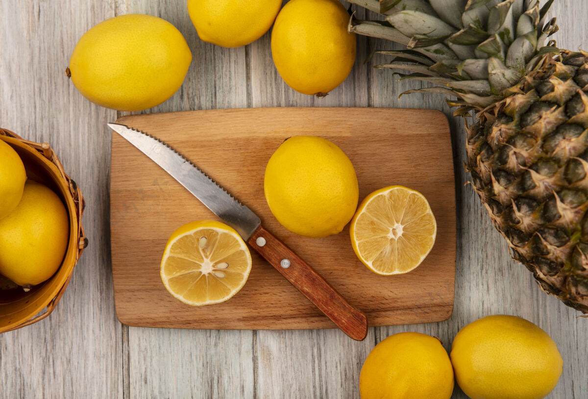柑橘新鲜的半个柠檬放在木制的厨房板上 刀子上放着柠檬 桶上放着柠檬和菠萝 隔离在灰色的木制表面上板块美味