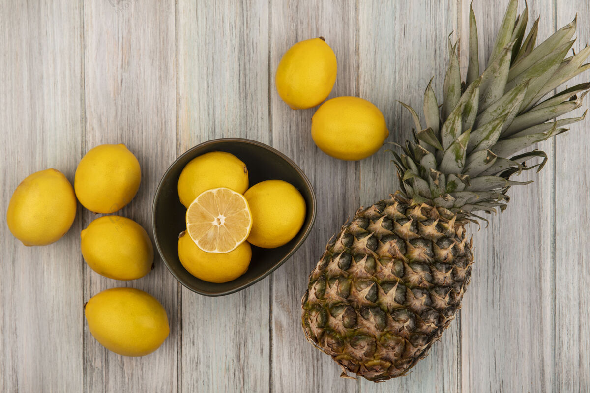 健康顶视图新鲜多汁的柠檬与菠萝和柠檬隔离在一个灰色的木制表面碗饮食块美味