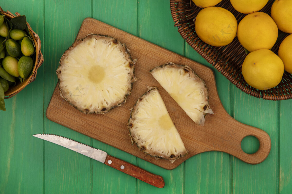 营养新鲜菠萝的顶视图在一个木制的厨房板上 刀子上有金盏花 桶上有柠檬 桶上有绿色的木制表面美味美味菠萝