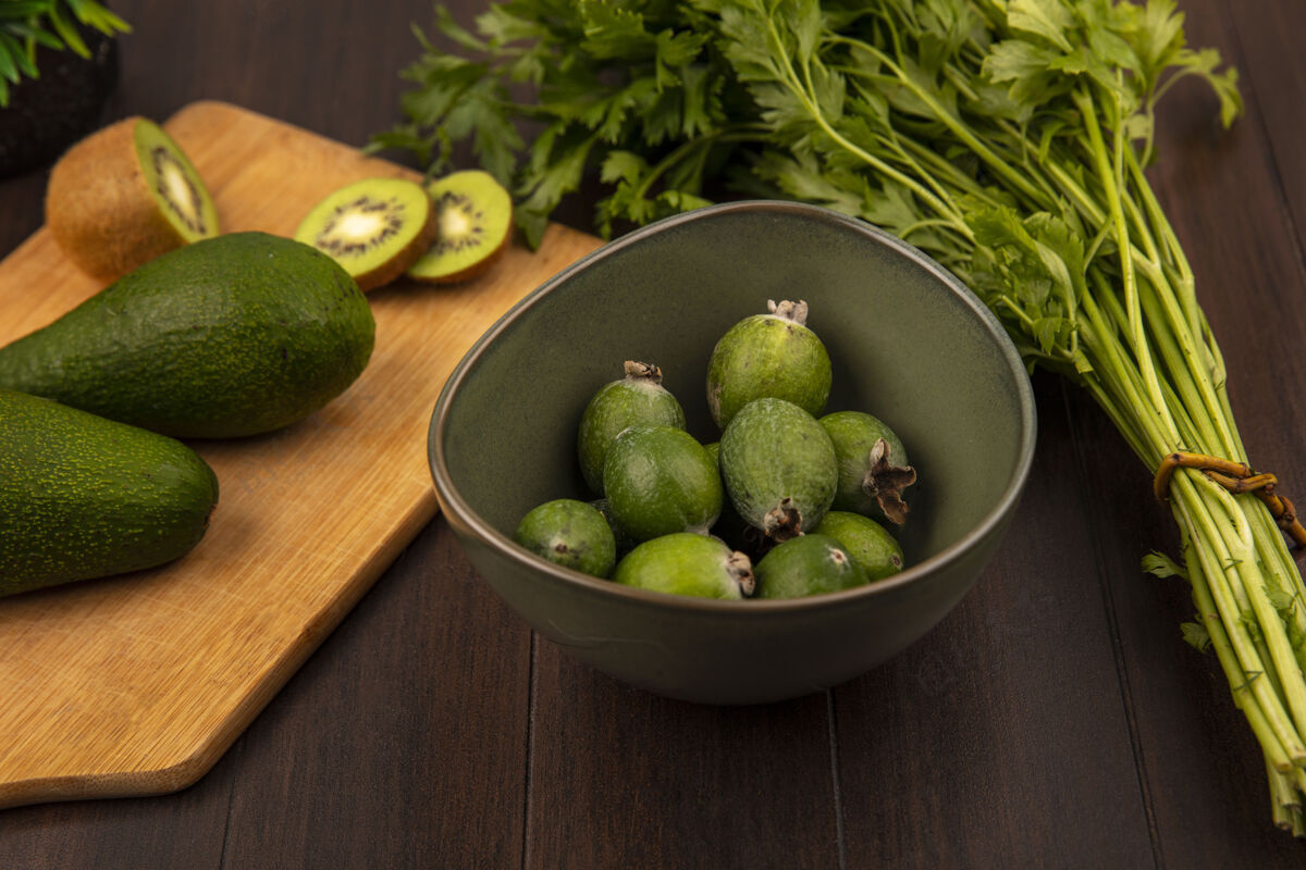一餐木制厨房板上梨形鳄梨的俯视图 碗上放着几片猕猴桃和芹菜 欧芹孤立在木制表面蔬菜午餐欧芹