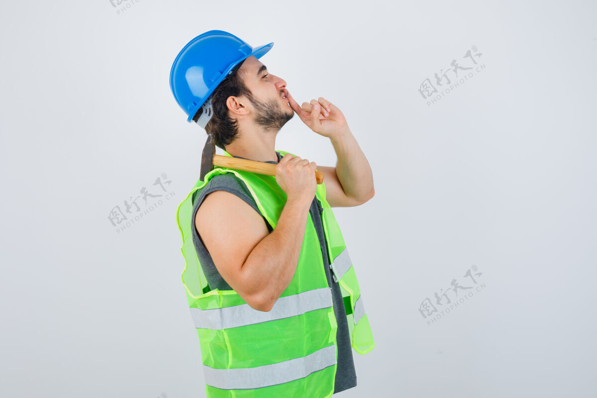 人年轻的建筑工人穿着工装 肩上扛着锤子 同时表现出沉默的姿态 仔细地看着前方秀头发男孩