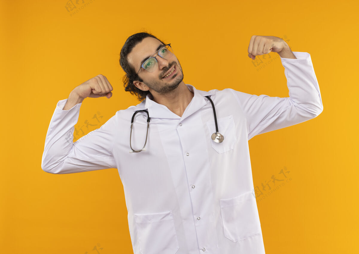 强壮看着身边高兴的年轻医生戴着医用眼镜 穿着医用长袍 手持听诊器 显示出强烈的姿态医生展示佩戴
