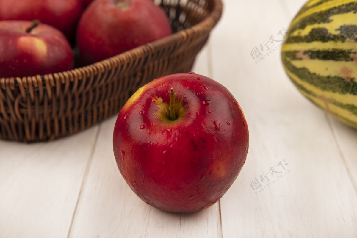 瓜顶视图是一个新鲜的红苹果 苹果放在一个桶里 哈密瓜放在一个白色的木制表面上木材美味水果
