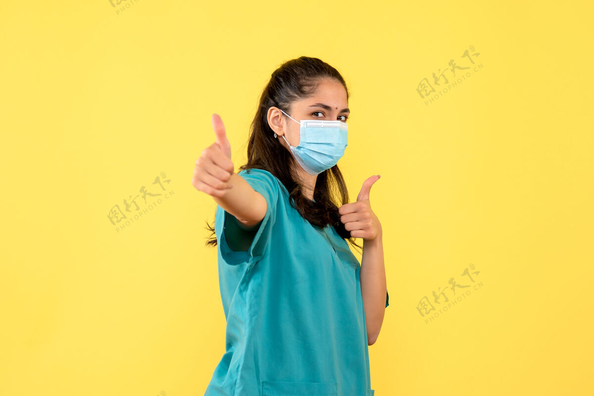 女士正面图美丽的女医生穿着制服 站在黄色的背景上竖起大拇指女医生表情正面