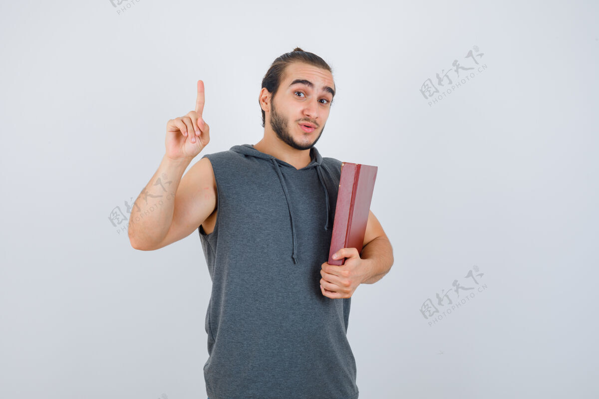 西装年轻的男性拿着书 指着无袖连帽衫 看起来很自信 正面视图严肃现代模特
