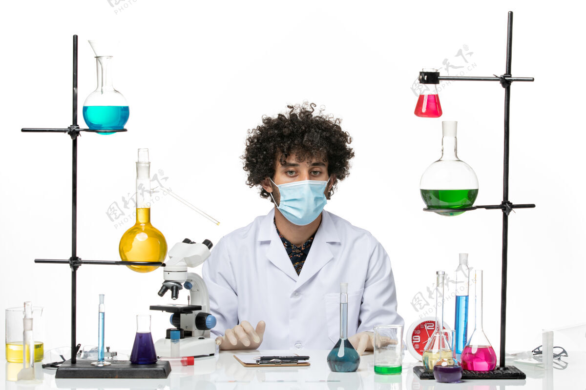实验室正面图：男药剂师穿着医疗服 戴着口罩 坐在不同的溶液中 空白处医生解决方案外套