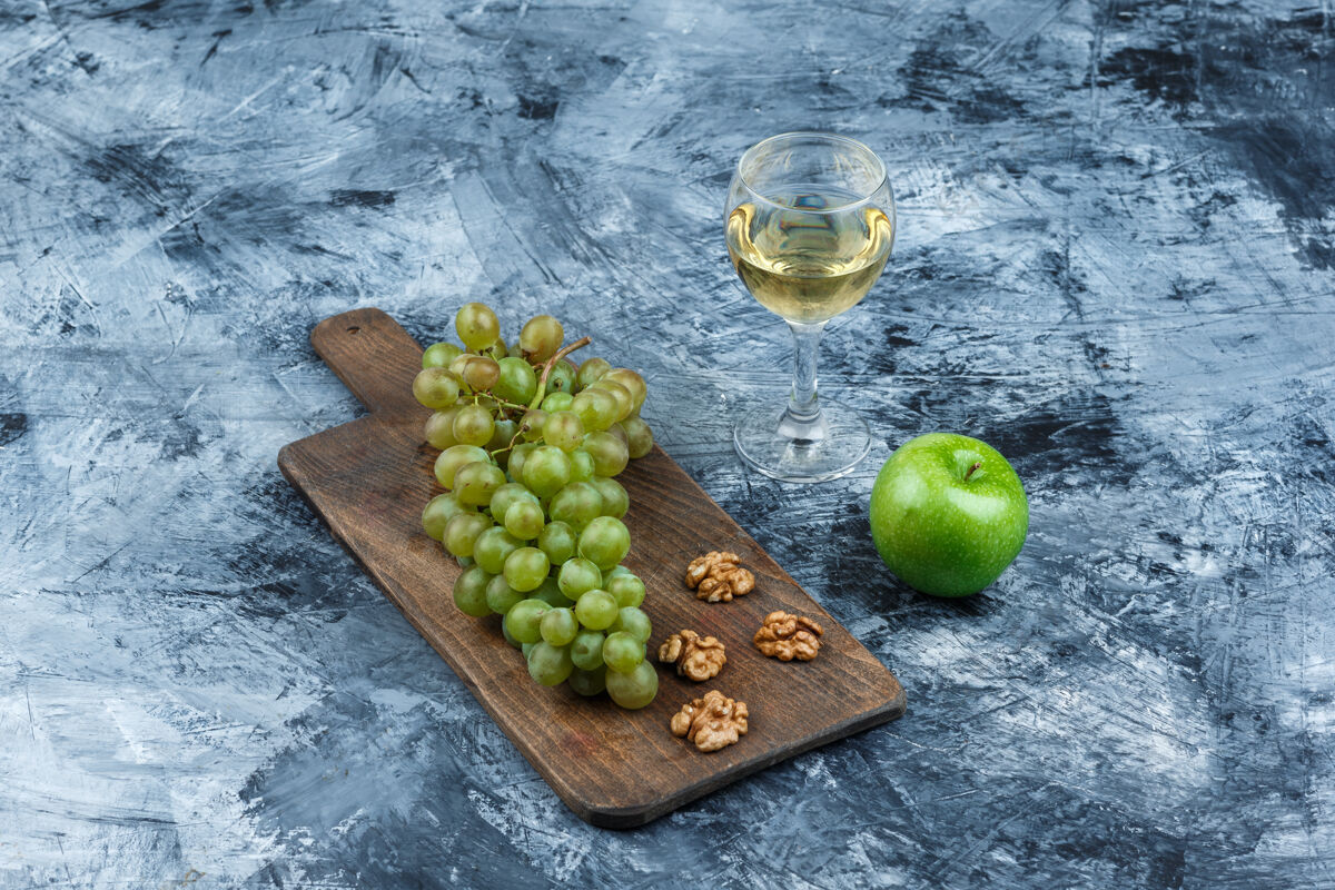 成熟高角度观看白葡萄 切菜板上的核桃和威士忌 深蓝色大理石背景上的青苹果水平酒庄葡萄酒新鲜