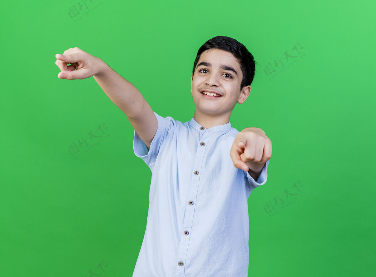 男人微笑着的年轻白人男孩看着并指着隔离在绿色墙上的复制空间表达手势指点
