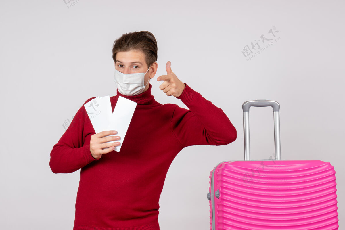 快乐戴着面具的年轻男子在白墙上拿着飞机票的正视图流行病夏天机票