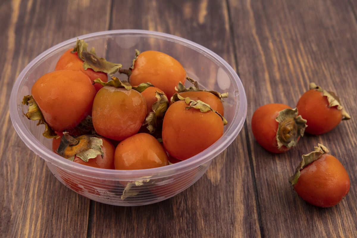 美味木制表面上透明塑料碗上柔软多汁的柿子俯视图新鲜午餐碗