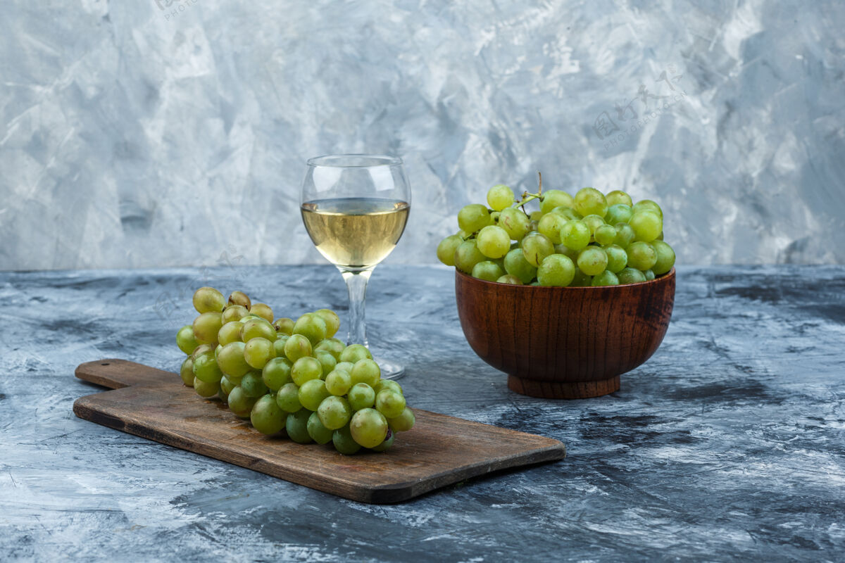 碗用一杯葡萄酒把白葡萄放在碗里 葡萄放在深蓝色大理石背景的砧板上水平串秋天葡萄酒