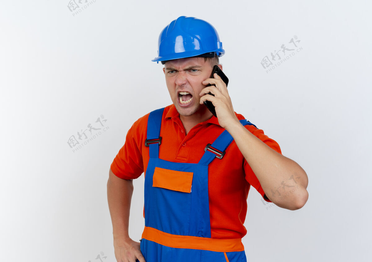 男性愤怒的年轻男性建筑工人穿着制服 戴着安全帽在电话里讲话建筑工人制服安全