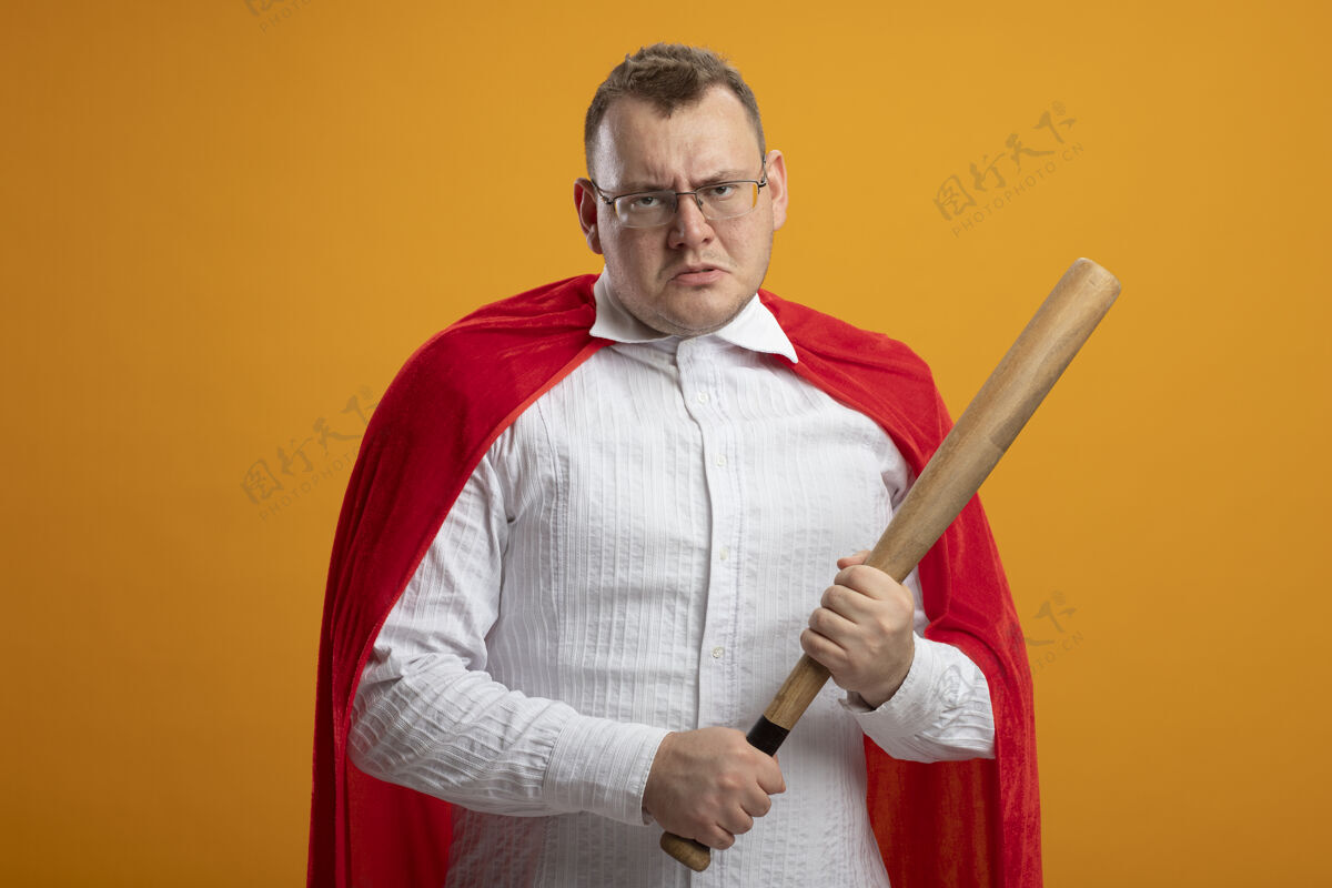 超级英雄愁眉不展的成年斯拉夫超级英雄 身穿红色斗篷 戴着眼镜 拿着棒球棒 隔离在橙色的墙上 留着复印空间男人橙色皱眉