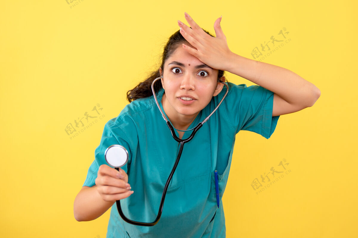 医疗器械年轻女医生的正视图 听诊器将手放在黄色墙上的头上护士医院手