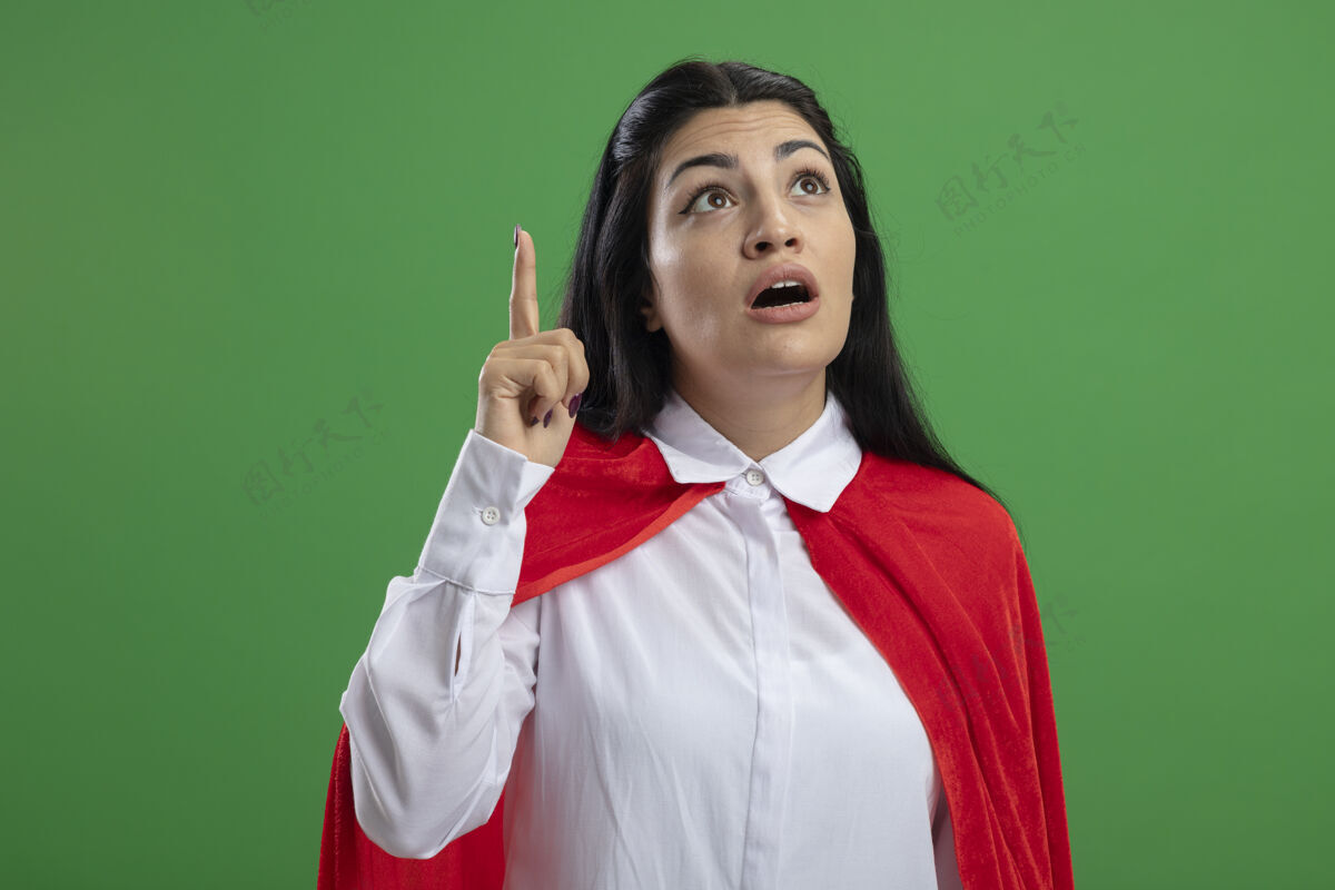 女孩令人印象深刻的年轻白种人超级英雄女孩举起食指 张口仰望隔离在绿色墙上的复制空间手指开放目录