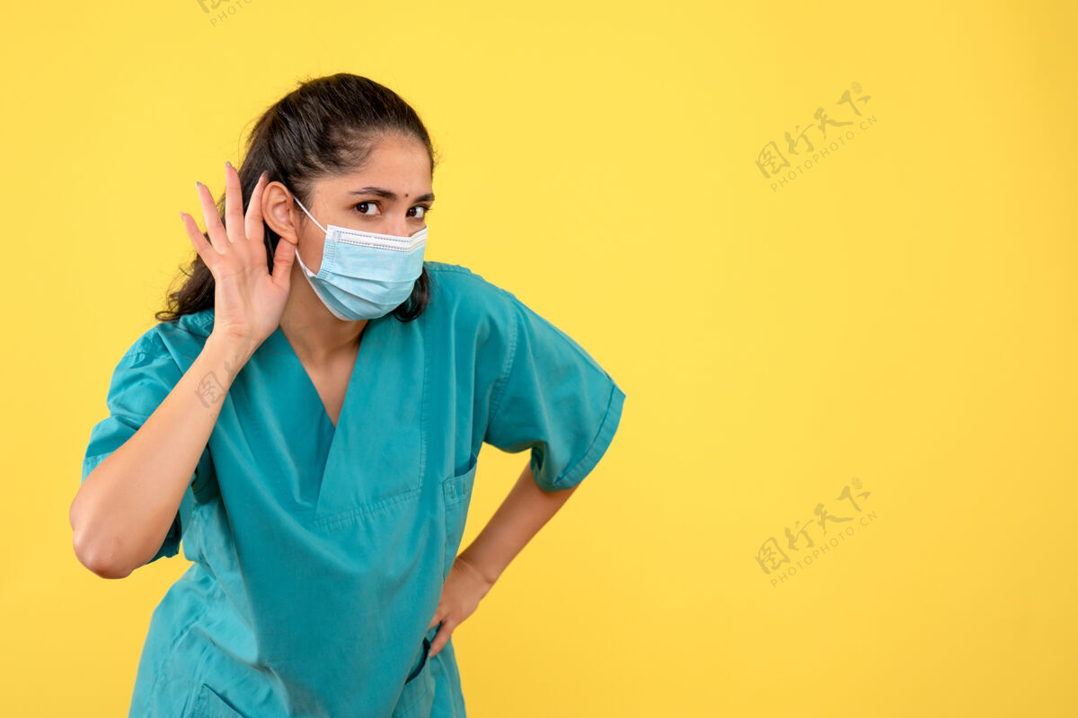 快乐戴着医用口罩的漂亮女医生正对着黄色墙上的东西听着呢医学肖像成人