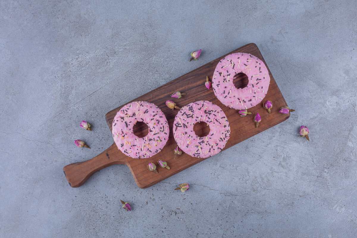 冰三个粉红色的甜甜圈 木质砧板上插着玫瑰美味美味甜甜圈