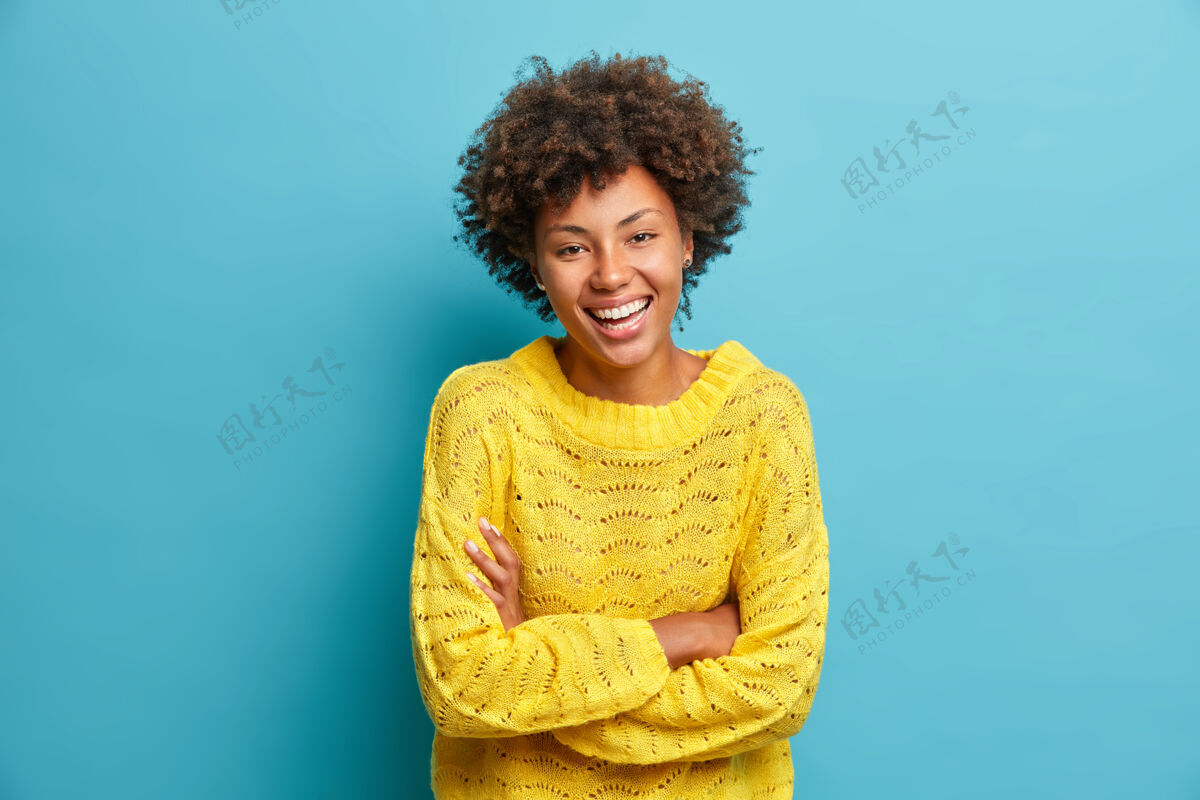 欢呼快乐快乐的女人快乐地笑着双臂合十 表达积极的情绪微笑着从快乐穿着休闲套头衫隔离在蓝色的墙上有乐趣或听到有趣的笑话人非洲姿势