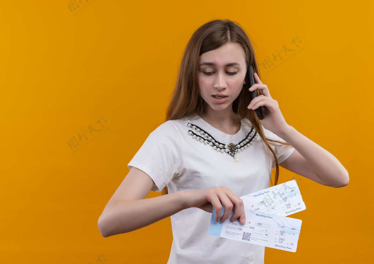 女人年轻的旅行家女孩一边打电话 一边拿着机票 一边低头看着隔离的橙色墙壁 墙上留着复印件放下按住年轻人