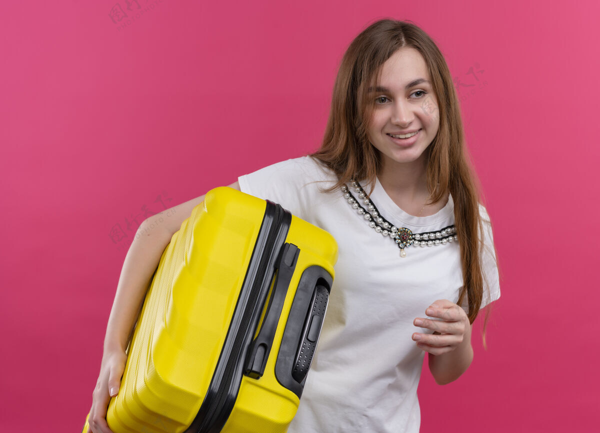 手提箱一个年轻的旅行家女孩把手提箱放在孤零零的粉红色墙上年轻人女人拿着
