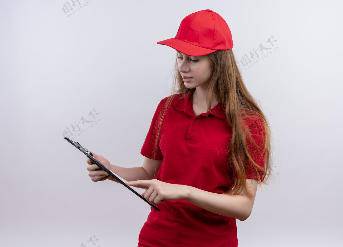 制服穿着红色制服的年轻女送货员把手指放在剪贴板上 看着孤立的白墙上剪贴板年轻分娩