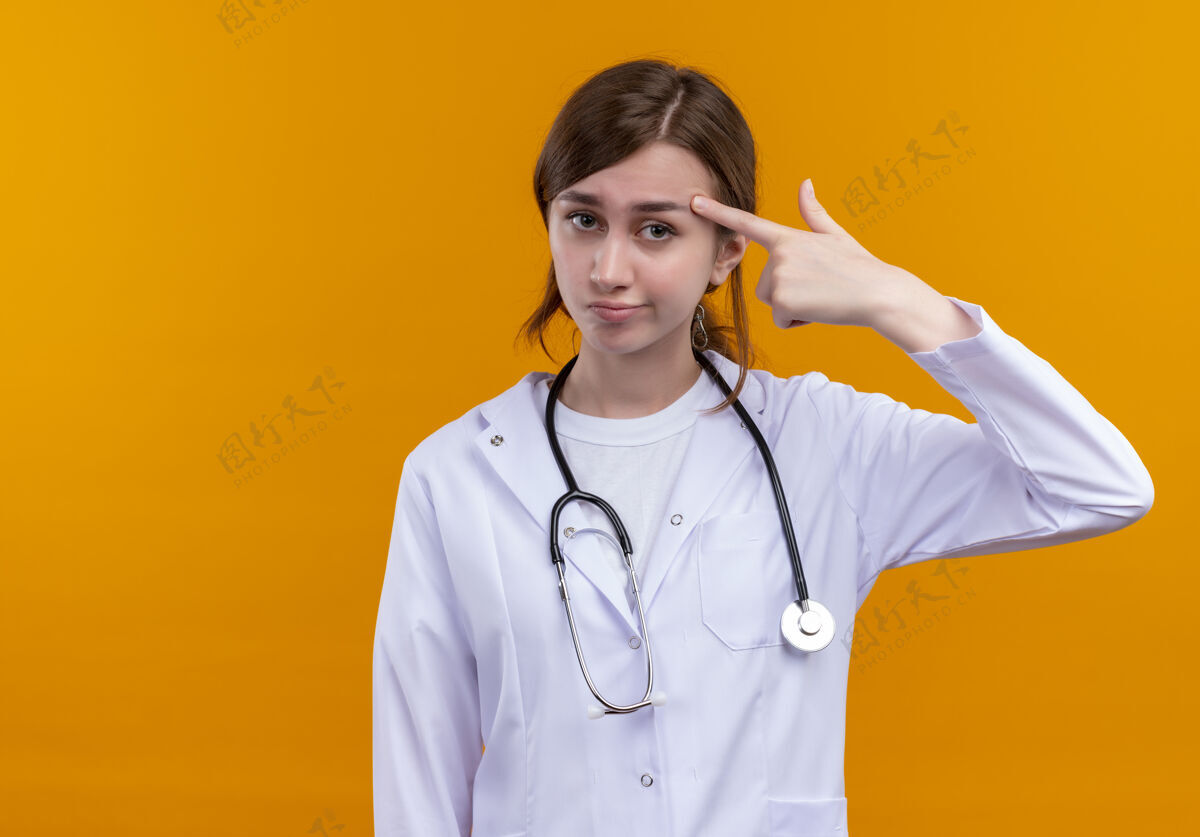 医生穿着医用长袍和听诊器的年轻女医生把手指放在隔离的橙色墙壁上的太阳穴上 并留有复印空间手指女人女人
