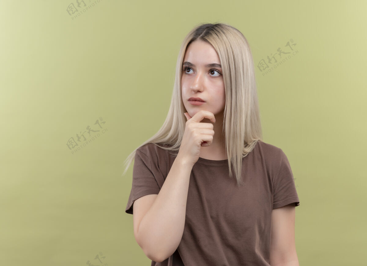 手体贴的年轻金发女孩把手放在下巴上的绿色隔离墙与复制空间心想年轻金发