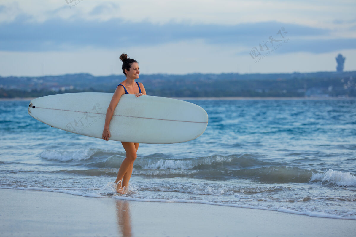 冲浪板美丽的女孩拿着冲浪板站在沙滩上人冲浪者性感