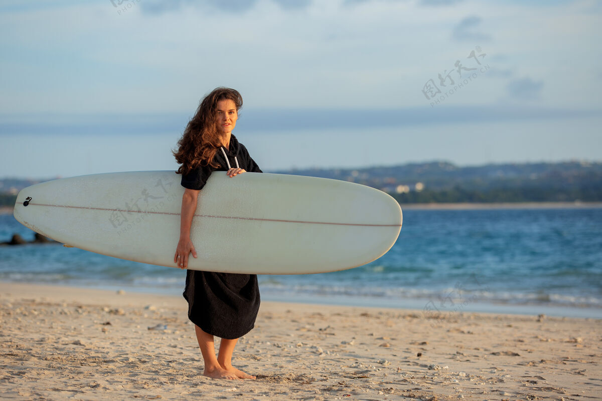 冲浪美丽的女孩拿着冲浪板站在沙滩上运动性感独自