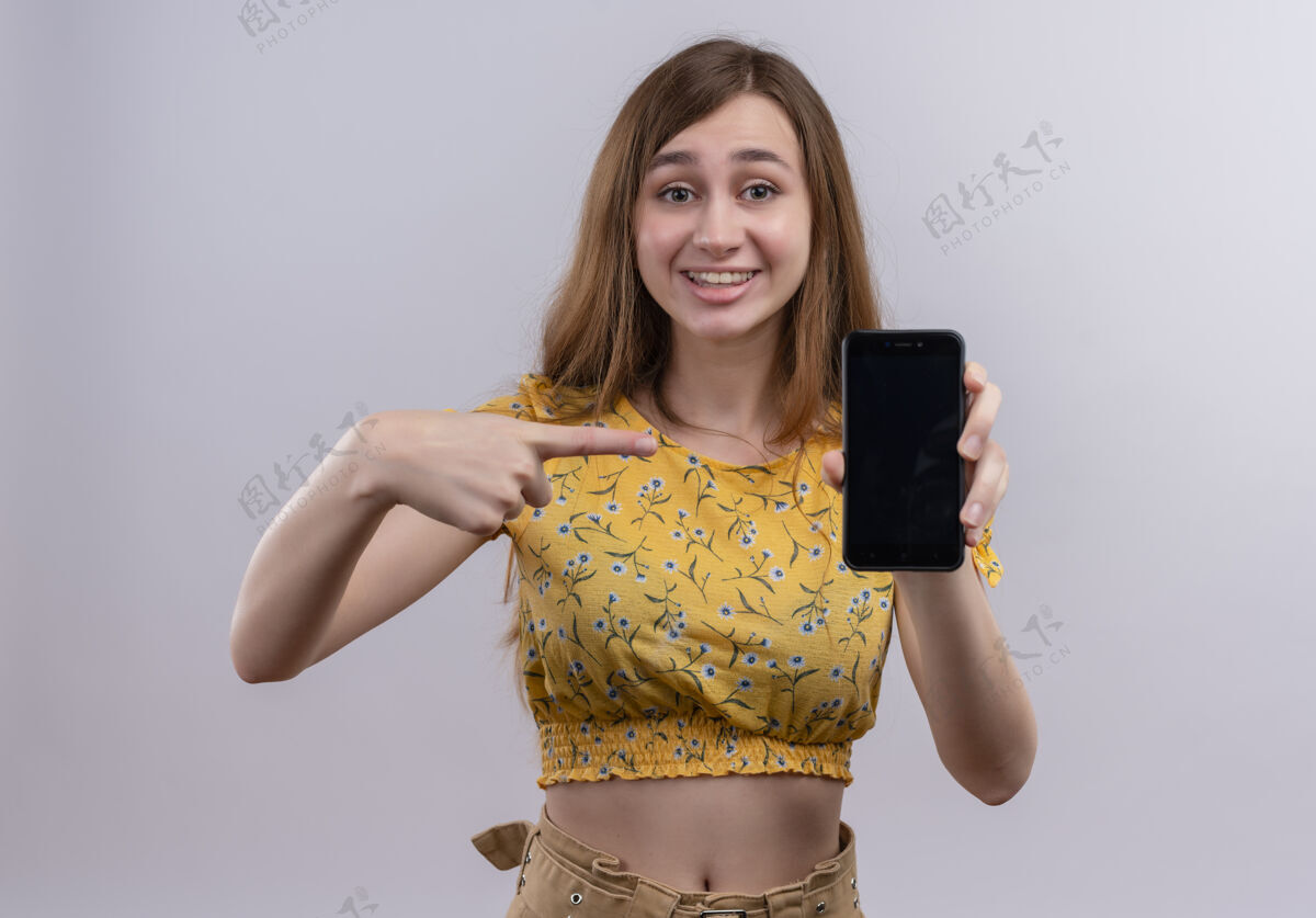 手机在孤零零的白墙上 微笑着拿着手机指着它的年轻女孩女孩电话女人