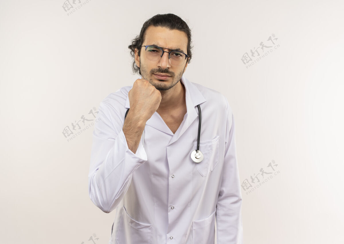 年轻严格的年轻男性医生 戴着眼镜 穿着白色长袍 手持听诊器 在隔离的白色墙壁上举起拳头 留有复印空间穿男性提高