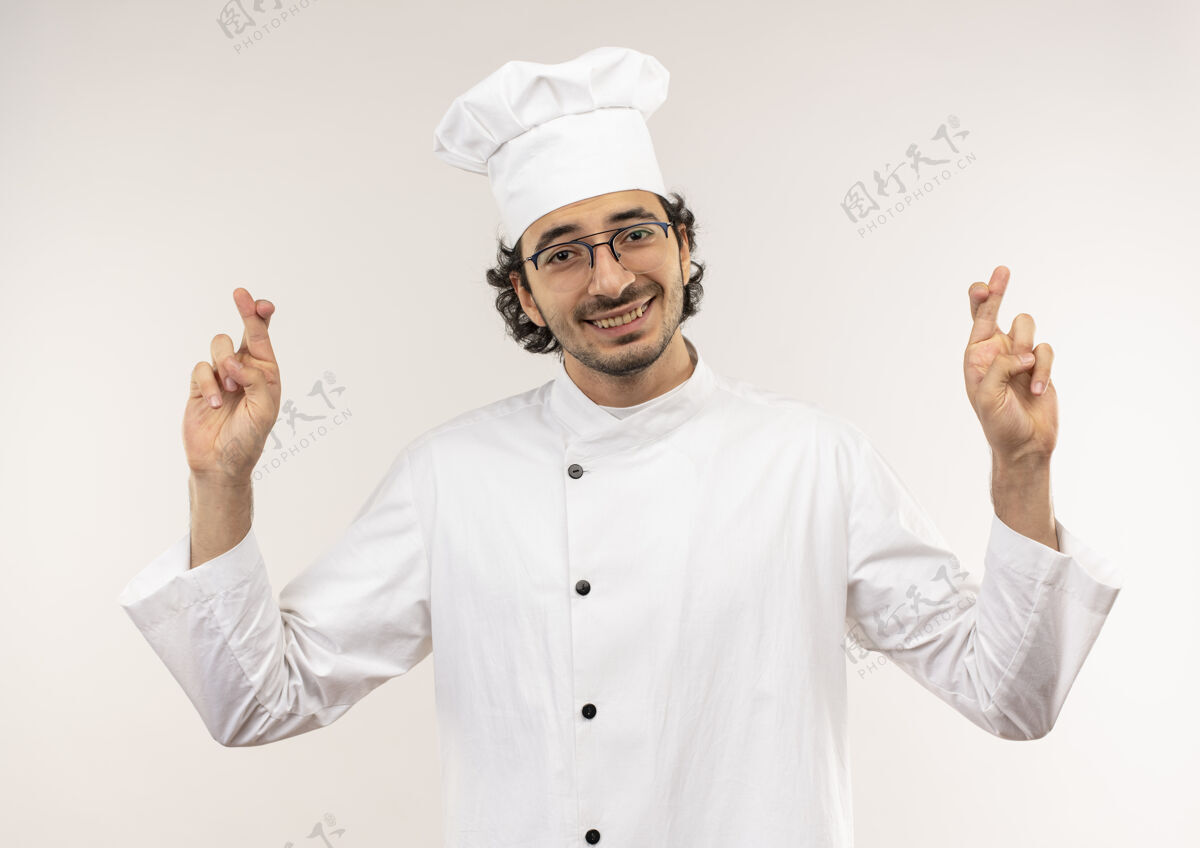 厨师面带微笑的年轻男厨师身穿厨师制服 戴着眼镜 手指交叉 孤立在白墙上穿眼镜烹饪