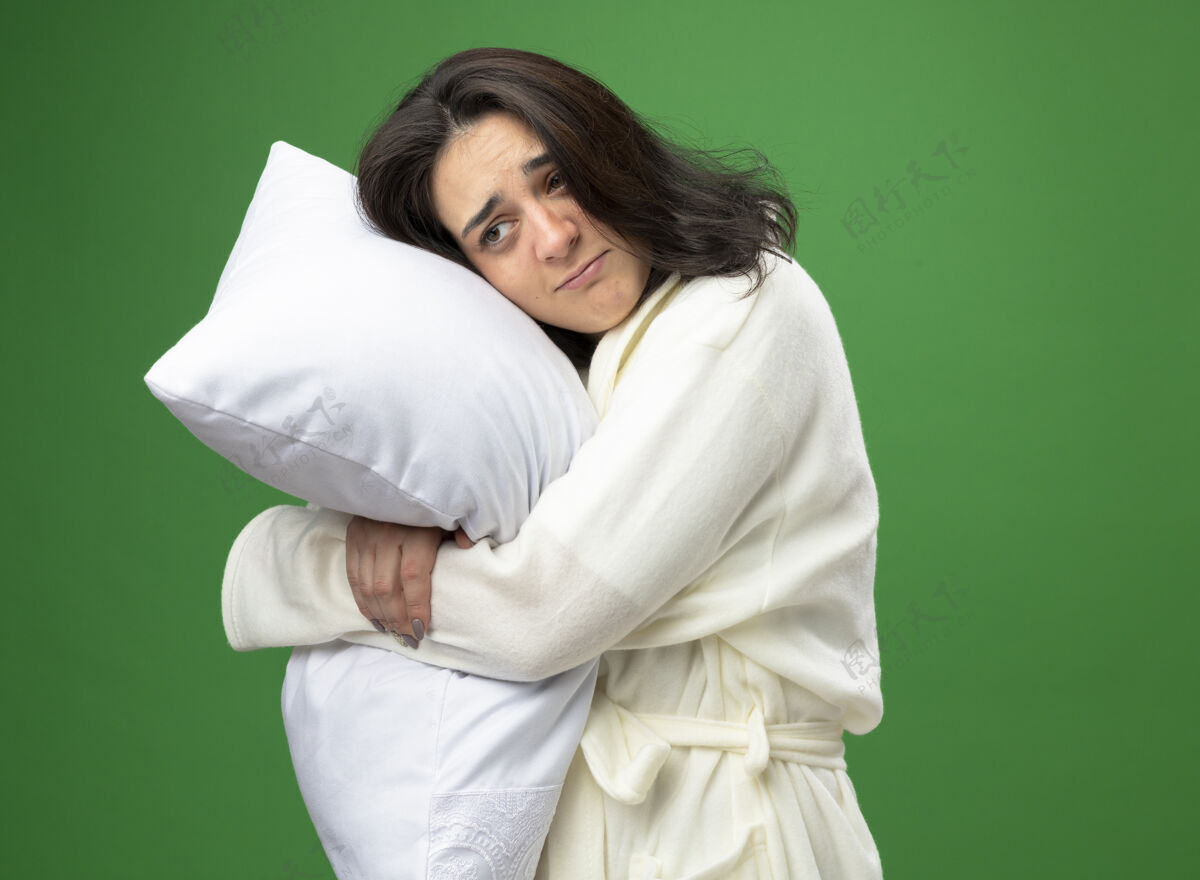 女孩穿着长袍站在侧视图中的年轻白种人病弱女孩抱着枕头 看起来笔直孤立 背景为绿色 有复制空间直站立拥抱